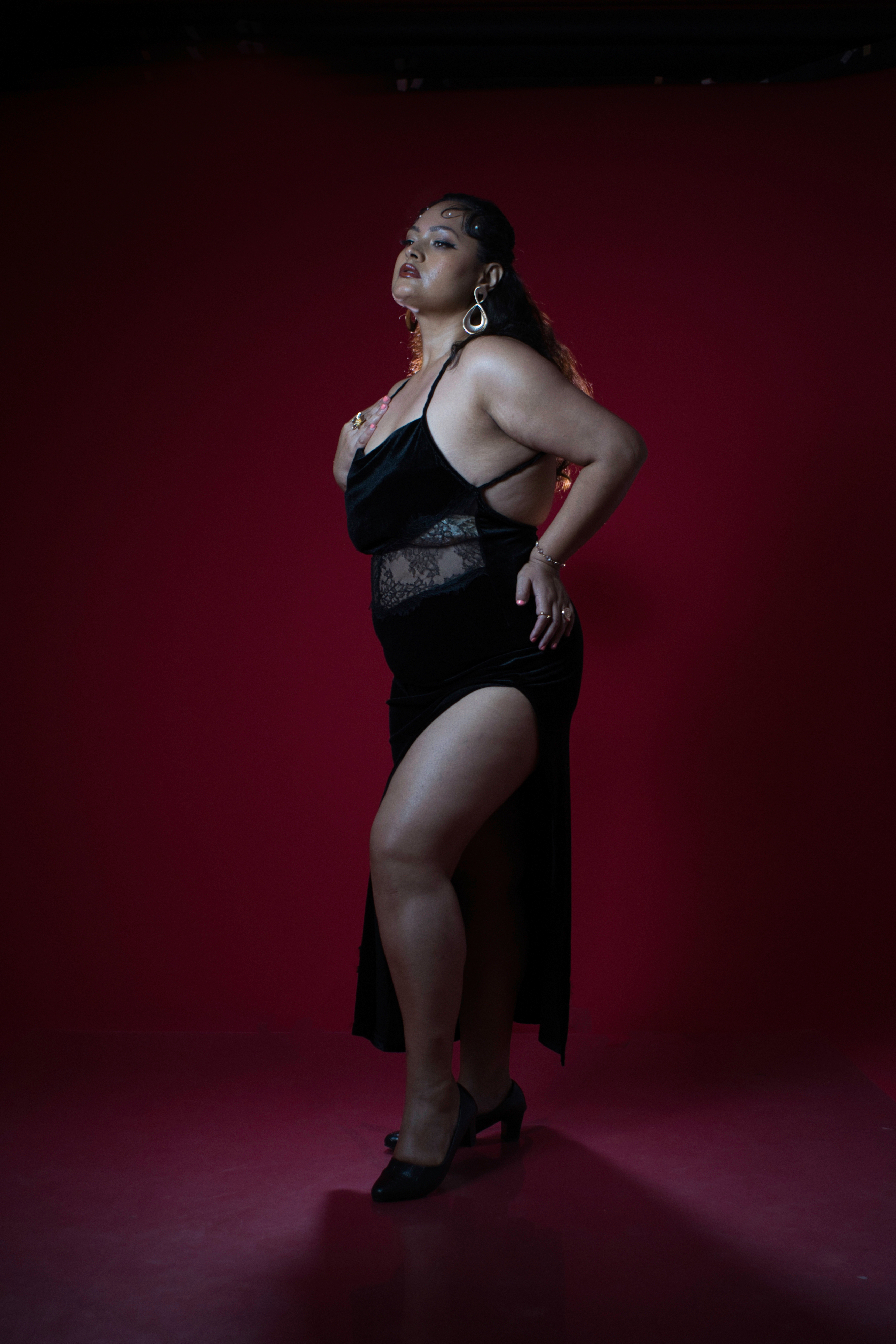 Model standing against a crimson backdrop in a black gown
