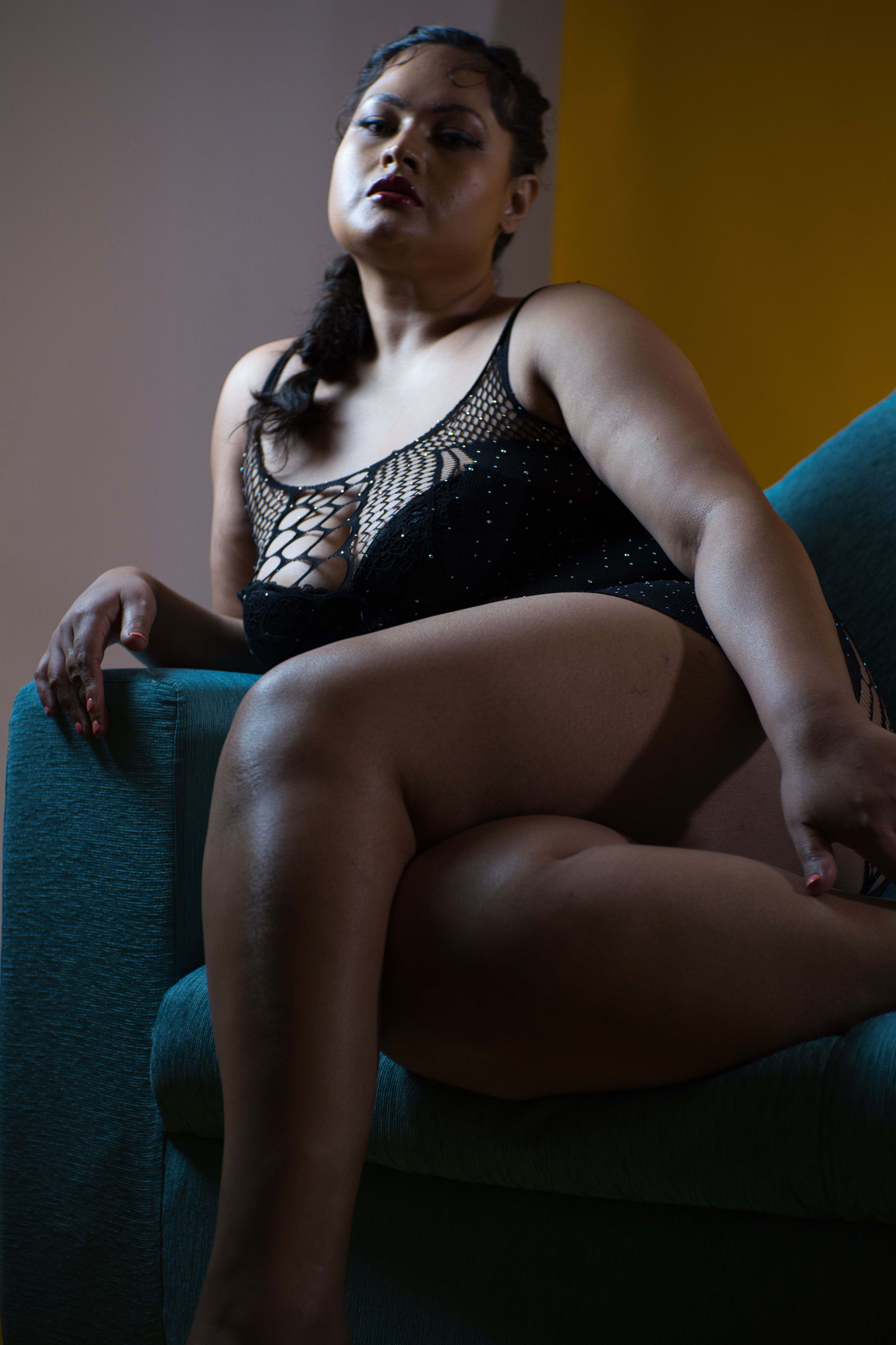 Model seated in a teal armchair under moody light